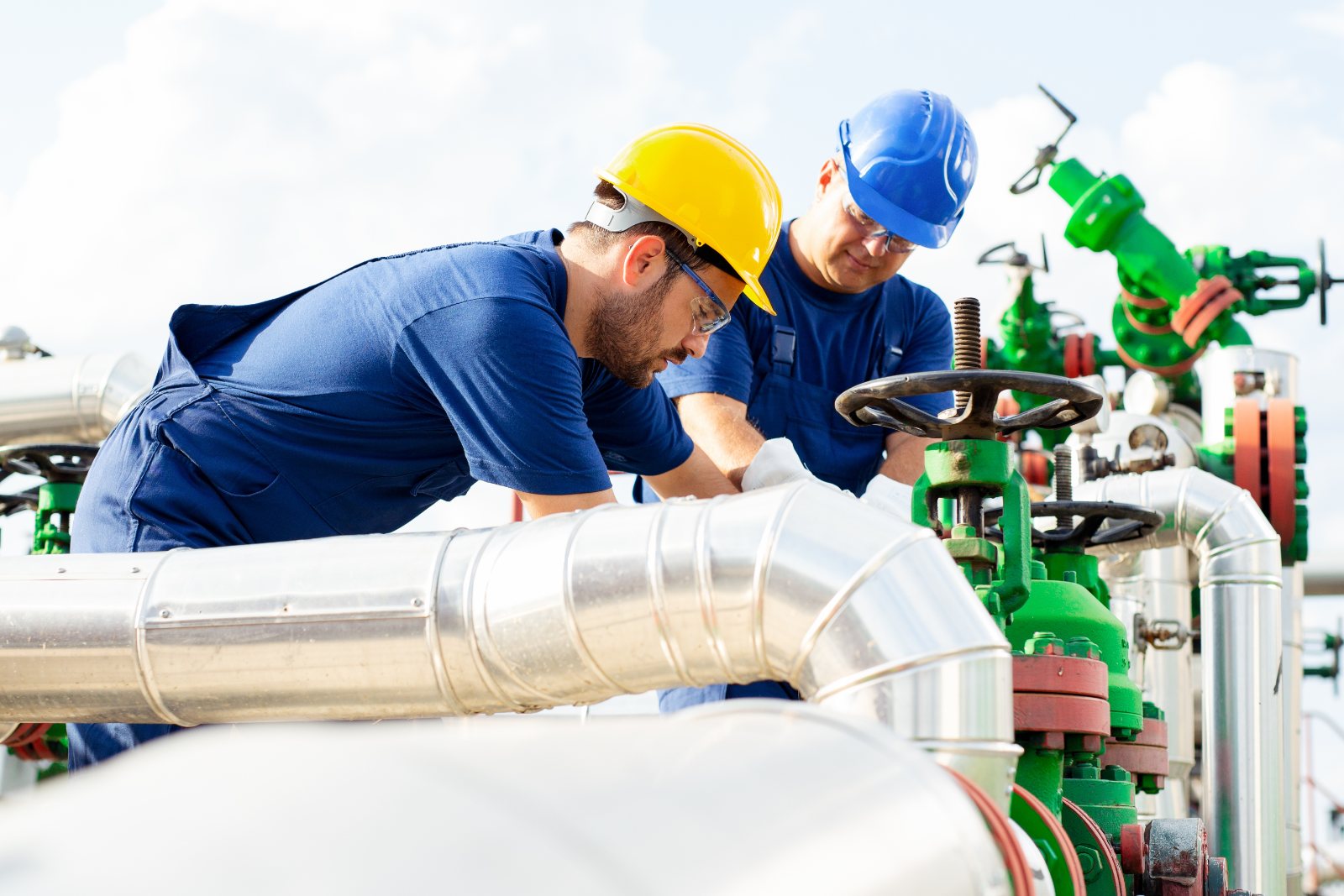 Two workers in hard hats inspecting a pipeline valve
